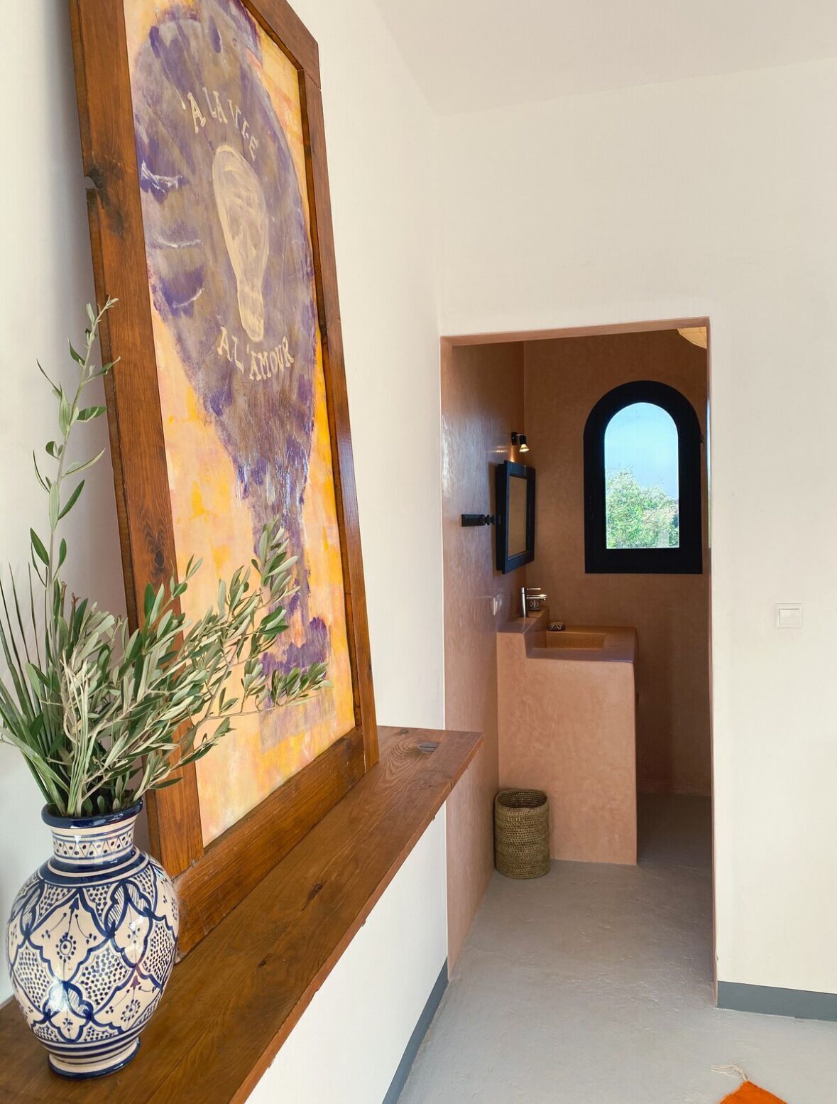 A hallway with a framed painting, a potted plant, and a small window.