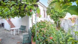 Un jardín con un banco, una mesa y una escalera que lleva a un edificio blanco con contraventanas rojas.