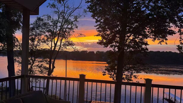 A covered deck with a view of a sunset over a body of water, surrounded by trees. - Lakefront - Sleeps 16 - Two Kitchens - Play Room (Union City)