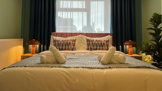 A neatly made bed with pillows, a bedside lamp, and a window with curtains.