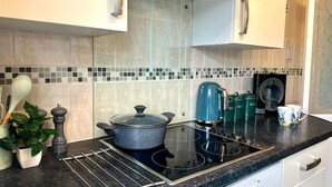 A kitchen with a black countertop, a stove, a kettle, and a coffee maker.