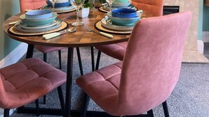 A dining area with a round table, pink chairs, and a television displaying 'NETFLIX' on the wall.