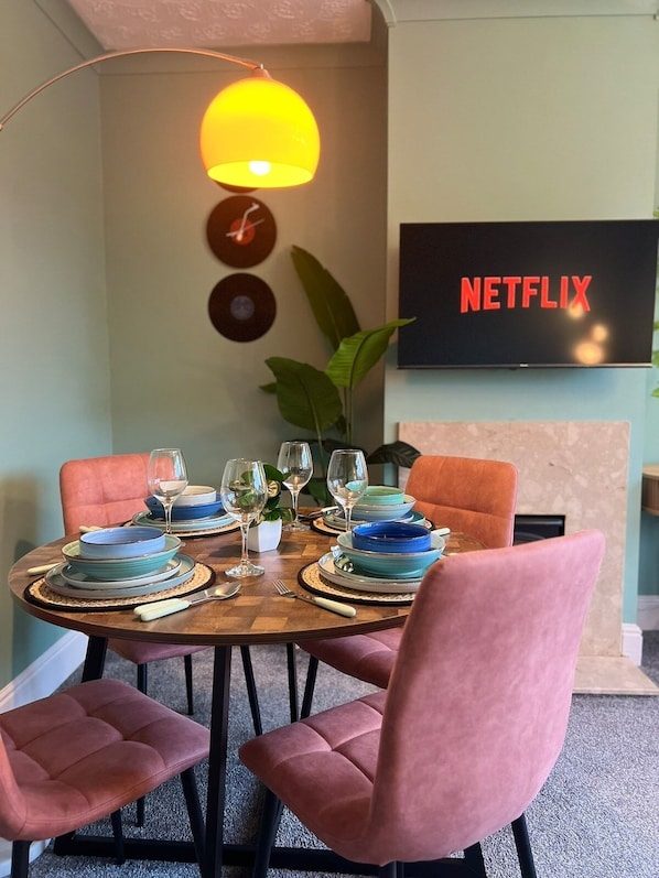 A dining area with a round table, pink chairs, and a television displaying 'NETFLIX' on the wall.