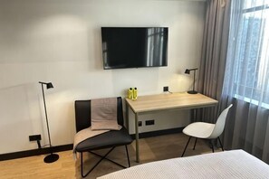 A hotel room with a bed, a desk with a chair, a TV, and a window with curtains. - ipartment Koeln Oper @HOME by Best Western (Cologne)