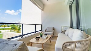 A balcony with wicker furniture, a small table, and a view of a pool and greenery. - Peace on The Beach in Punta Cana (Punta Cana)