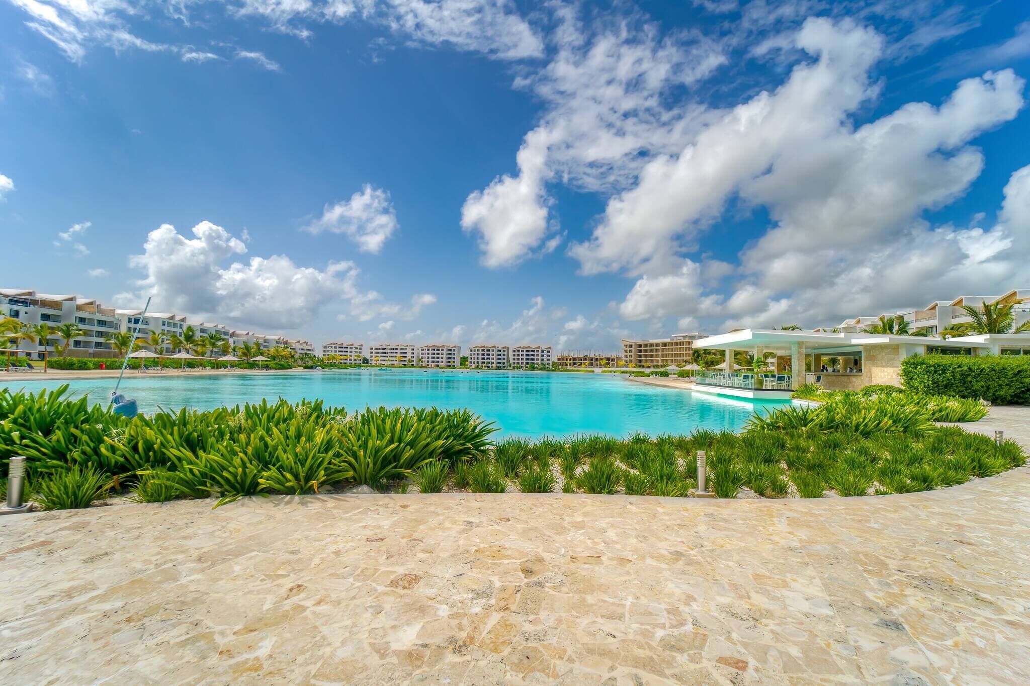 Ein Poolbereich eines Resorts mit blauem Himmel, umgeben von üppiger Vegetation und modernen Gebäuden.