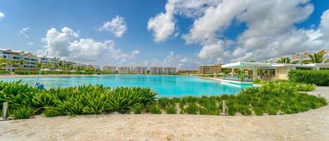 Ein Poolbereich eines Resorts mit blauem Himmel, umgeben von üppiger Vegetation und modernen Gebäuden.