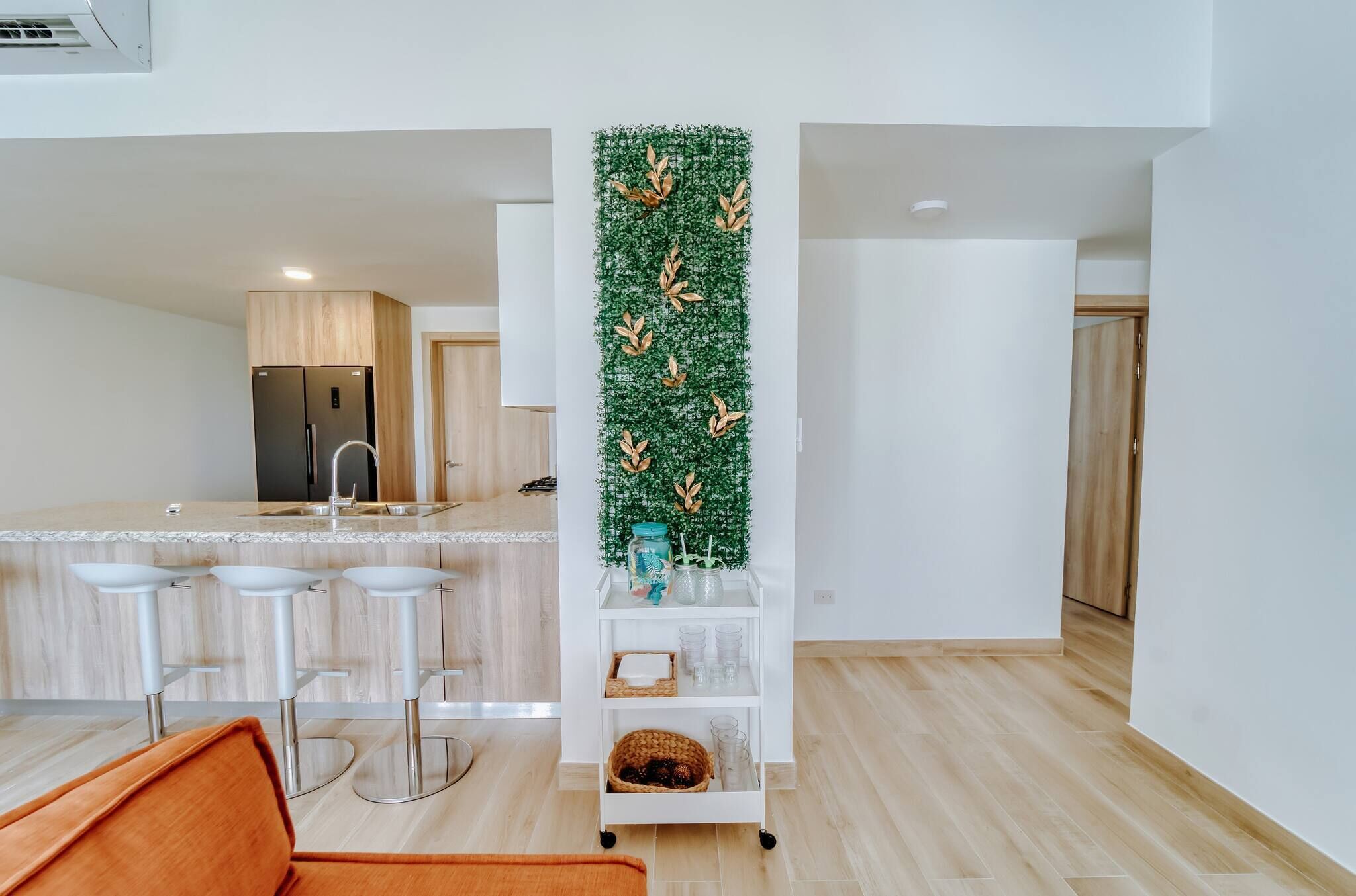 A modern kitchen with a central island, white bar stools, and a decorative vertical garden.