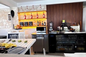 A modern bar area with a beverage dispenser, a microwave, and a variety of liquor bottles on shelves. - Peace on The Beach in Punta Cana (Punta Cana)