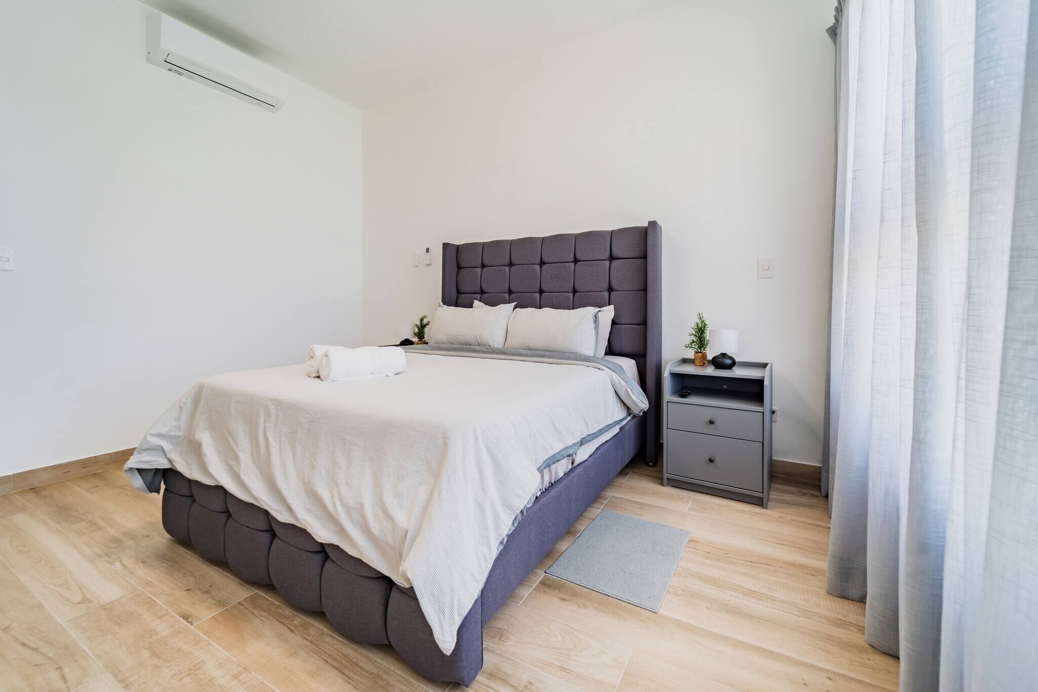 A modern bedroom with a large bed, a bedside table, and a small plant.