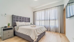 A modern bedroom with a large bed, a bedside table, and a window with sheer curtains. - Peace on The Beach in Punta Cana (Punta Cana)