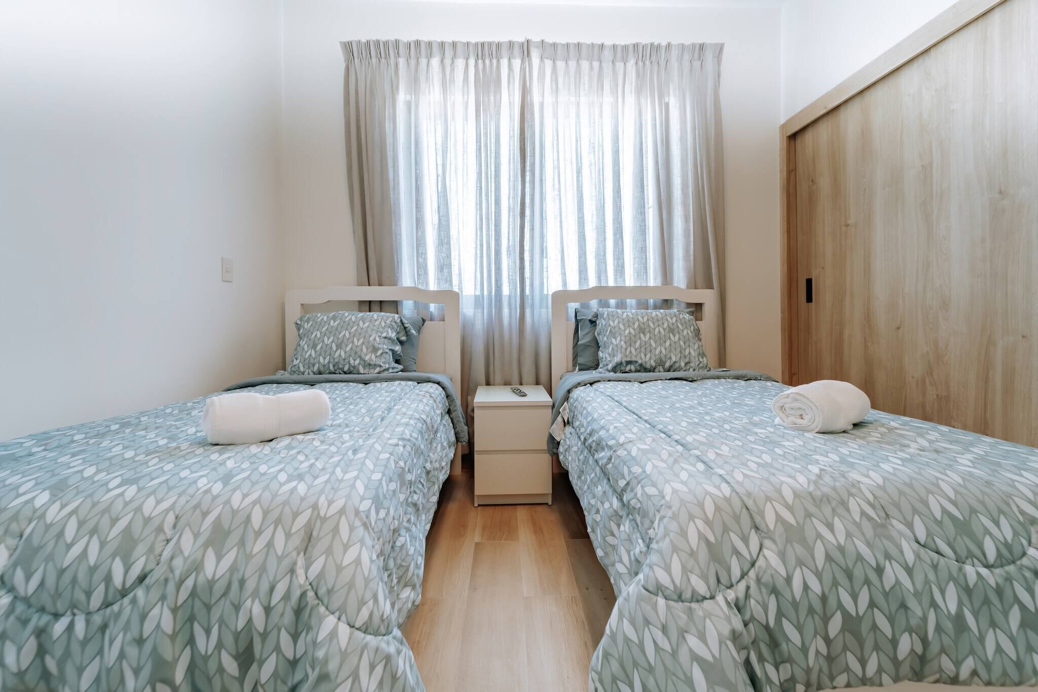 A bedroom with two single beds, a wooden wardrobe, and a nightstand between the beds.