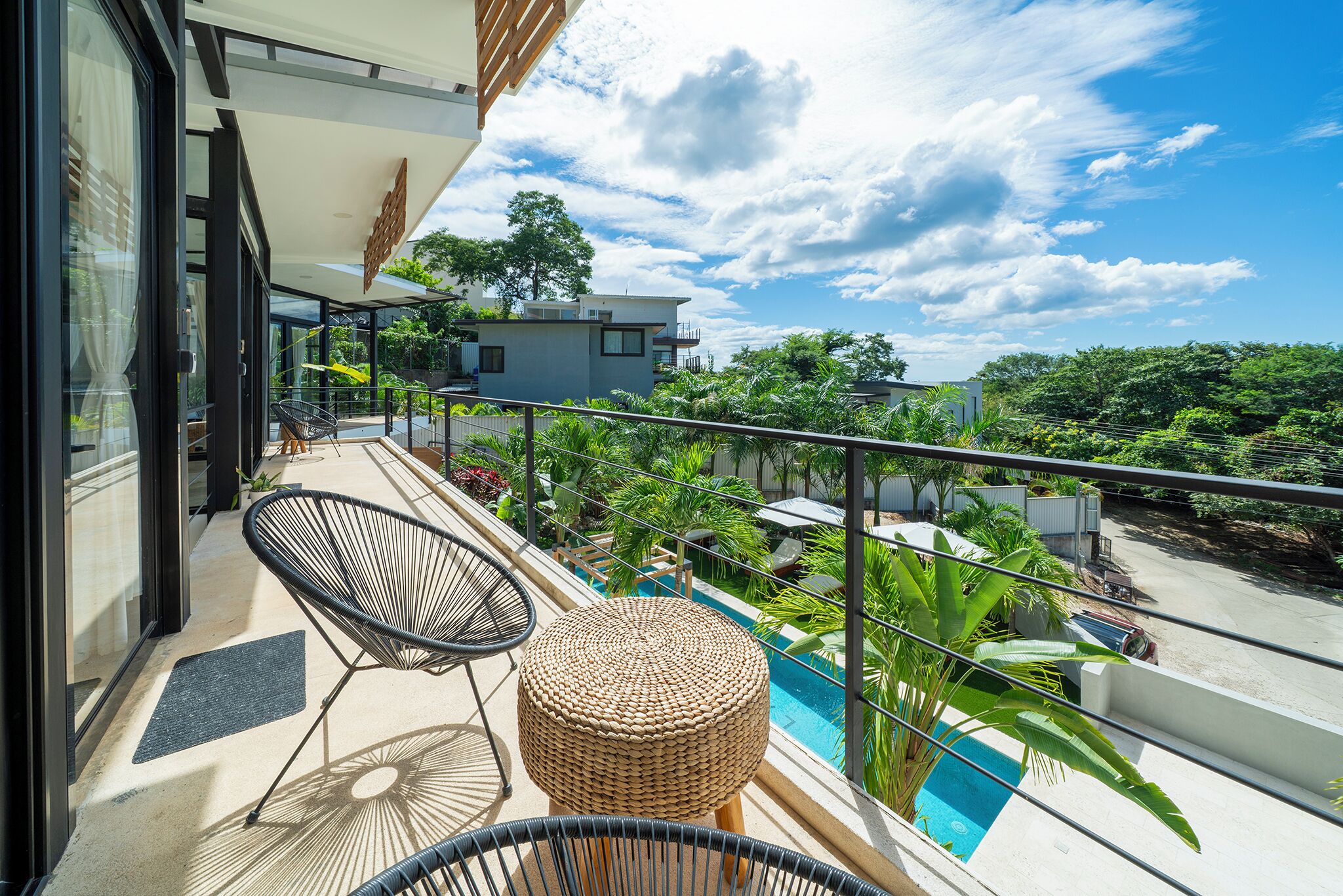 A balcony with a pool, wicker furniture, and a view of surrounding greenery.