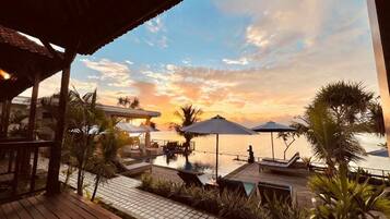 Zona de piscina en un resort con sombrillas, sillas reclinables y vista al atardecer sobre el agua.