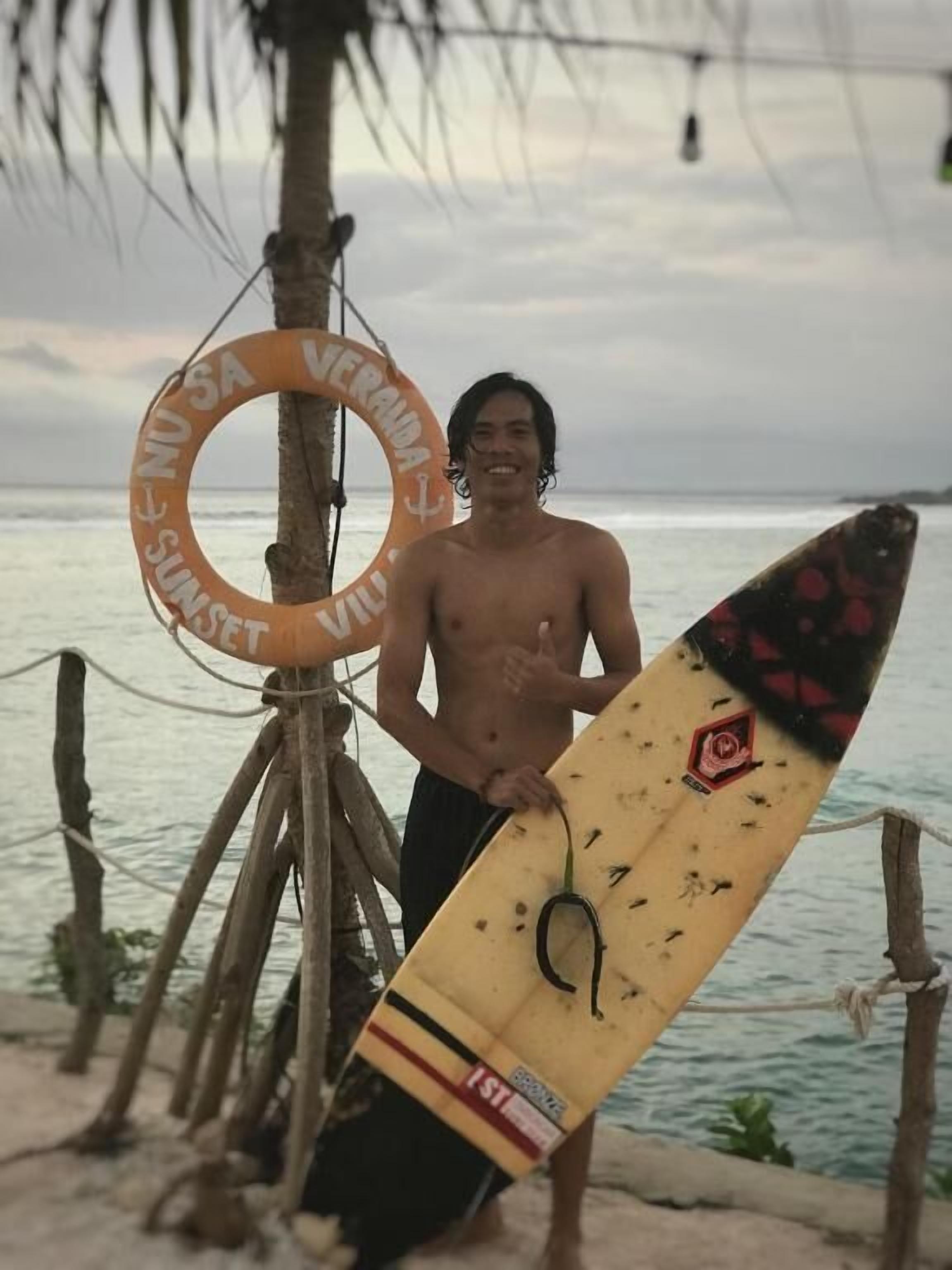 A person holding a surfboard near a lifebuoy on a beach.