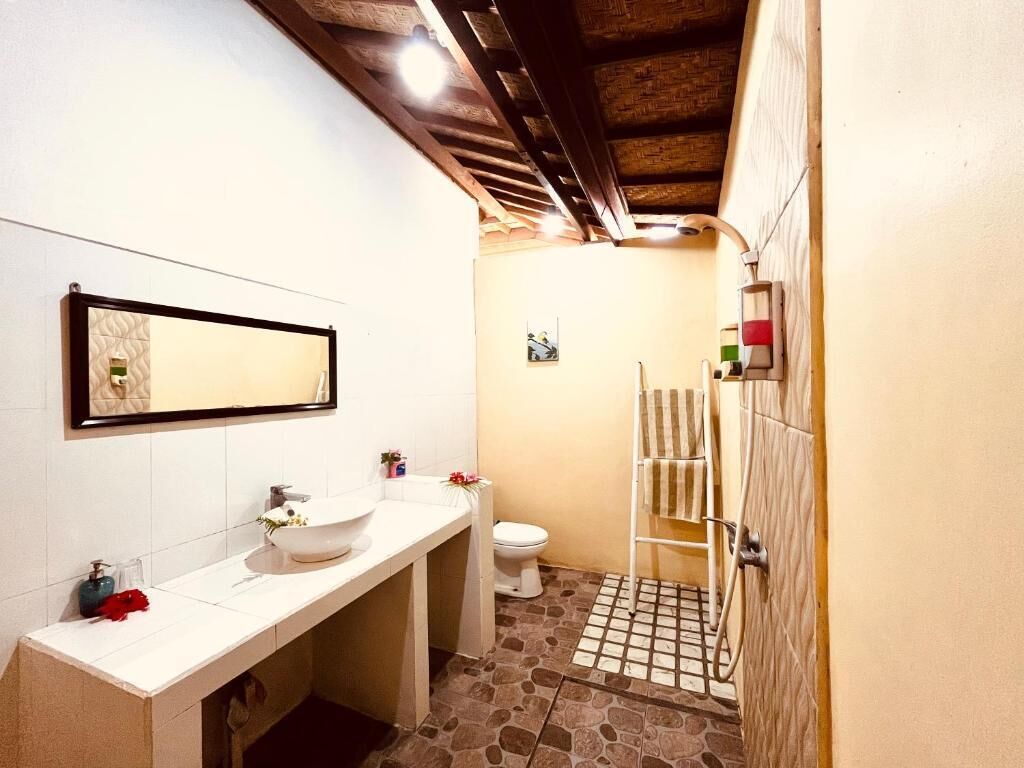 A bathroom with a white sink, mirror, and toilet. There is a shower area with a towel rack and a tiled floor.