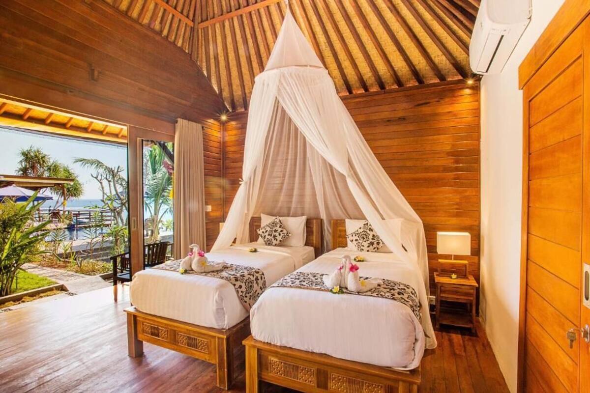 Quarto com duas camas, cada uma com dossel, piso de madeira e vista para o exterior.