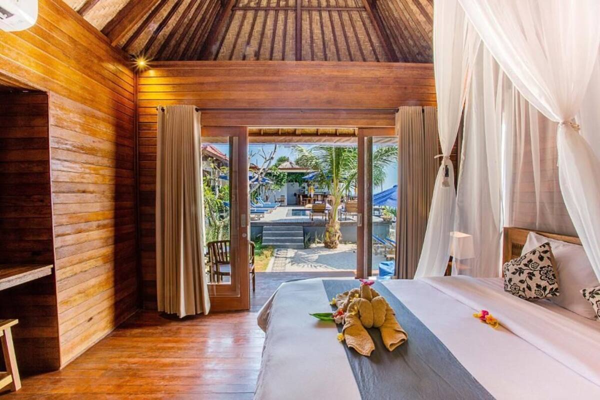 Quarto de madeira com cama, cortinas e vista para área externa com escadas e guarda-sóis.