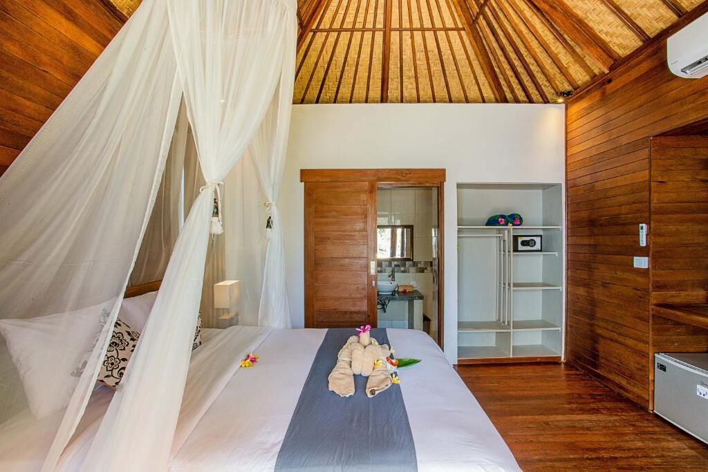 A bedroom with a canopy bed, wooden walls, and a kitchenette visible through an open door.