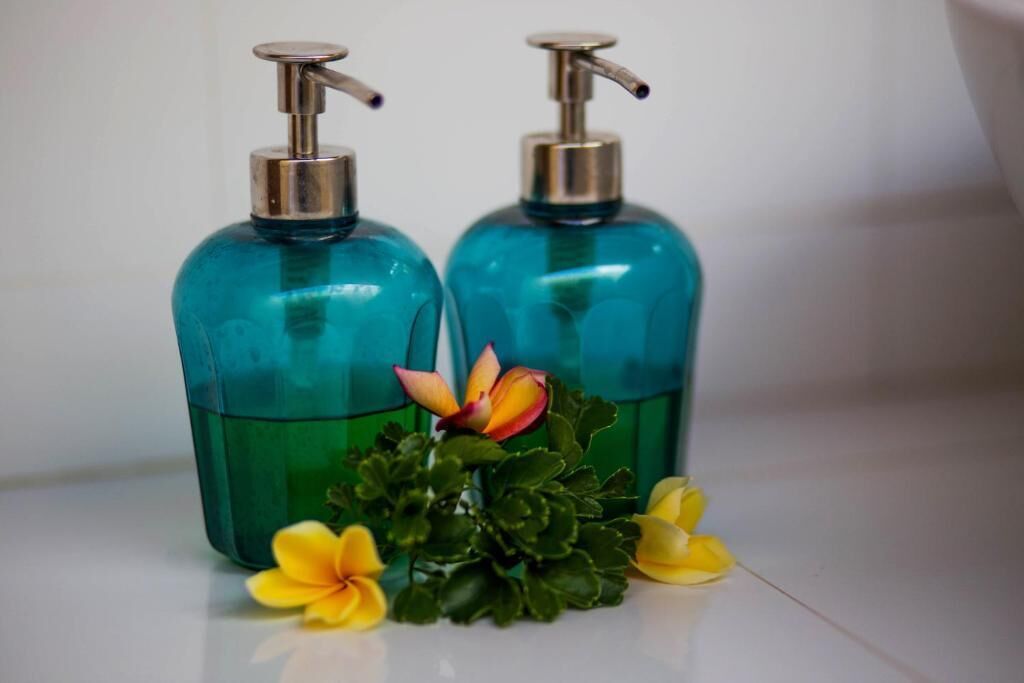 Two teal glass bottles with pumps, likely containing liquid soap, and a small green plant with yellow flowers.