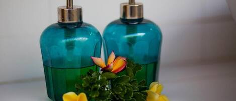 Two teal glass bottles with pumps, likely containing liquid soap, and a small green plant with yellow flowers.