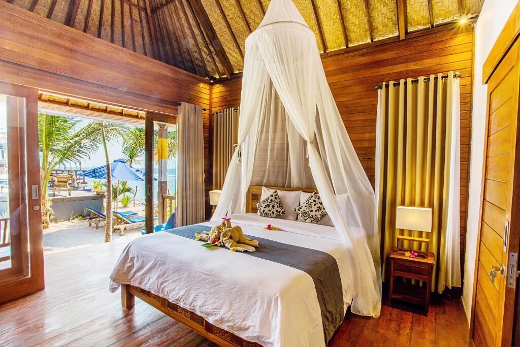 A bedroom with a canopy bed, wooden flooring, and a view of the beach.