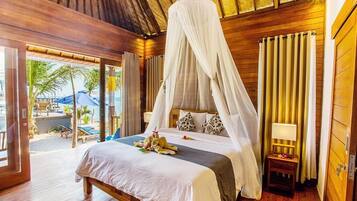 A bedroom with a canopy bed, wooden flooring, and a view of the beach.