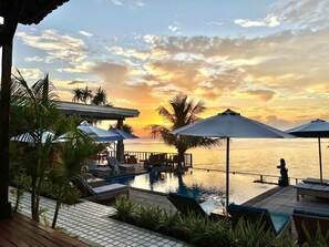 Zona junto a la piscina con sillas de descanso y sombrillas, con vista a un cuerpo de agua al atardecer.