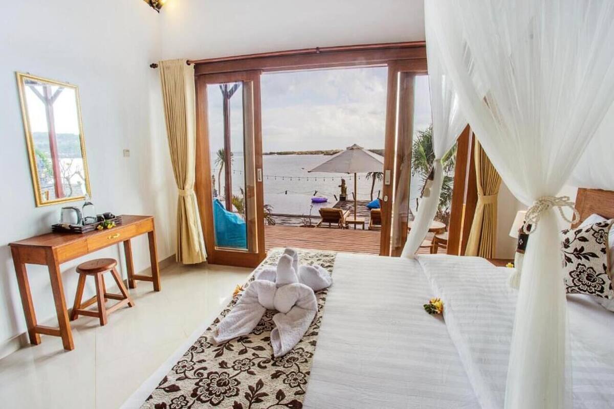 Quarto com cama, escrivaninha e vista para a praia.