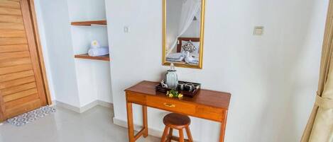 Quarto com escrivaninha de madeira, espelho, cama com dossel e prateleira pequena com toalhas.