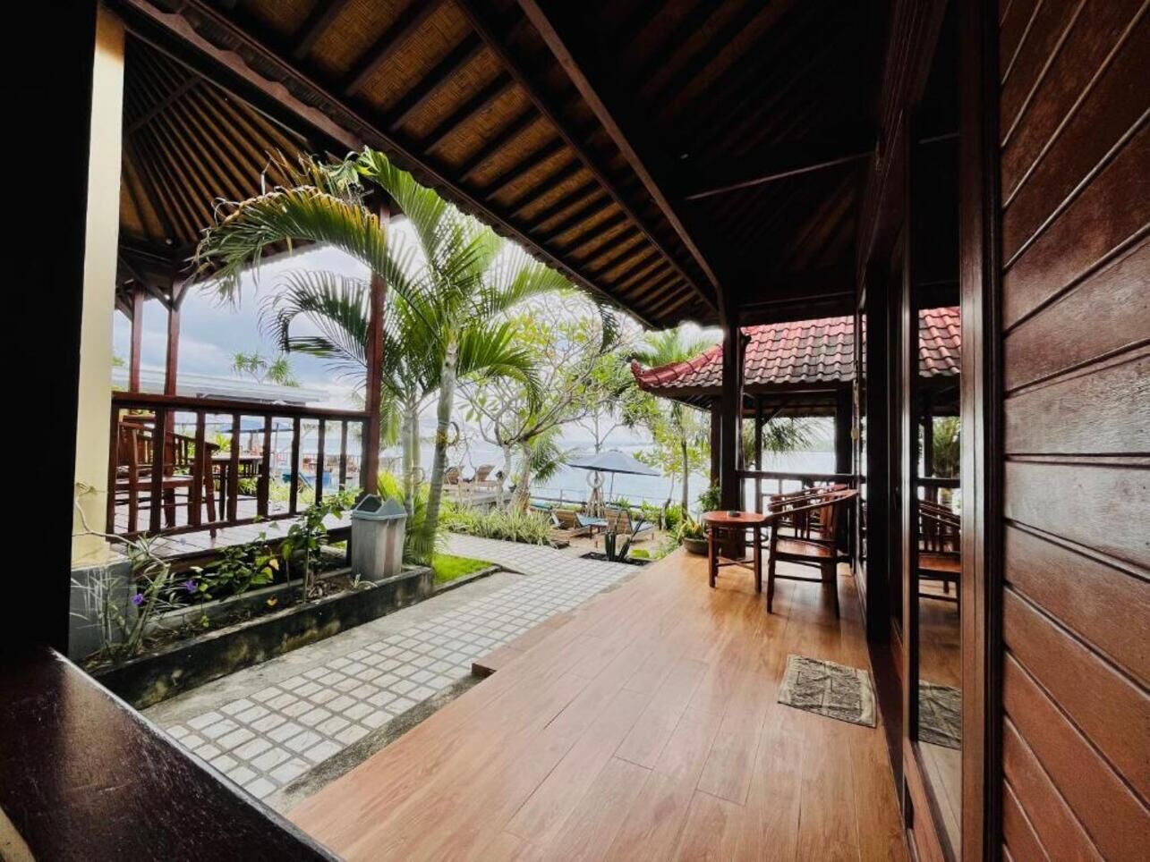 A wooden deck with outdoor seating, a view of the sea, and tropical plants.