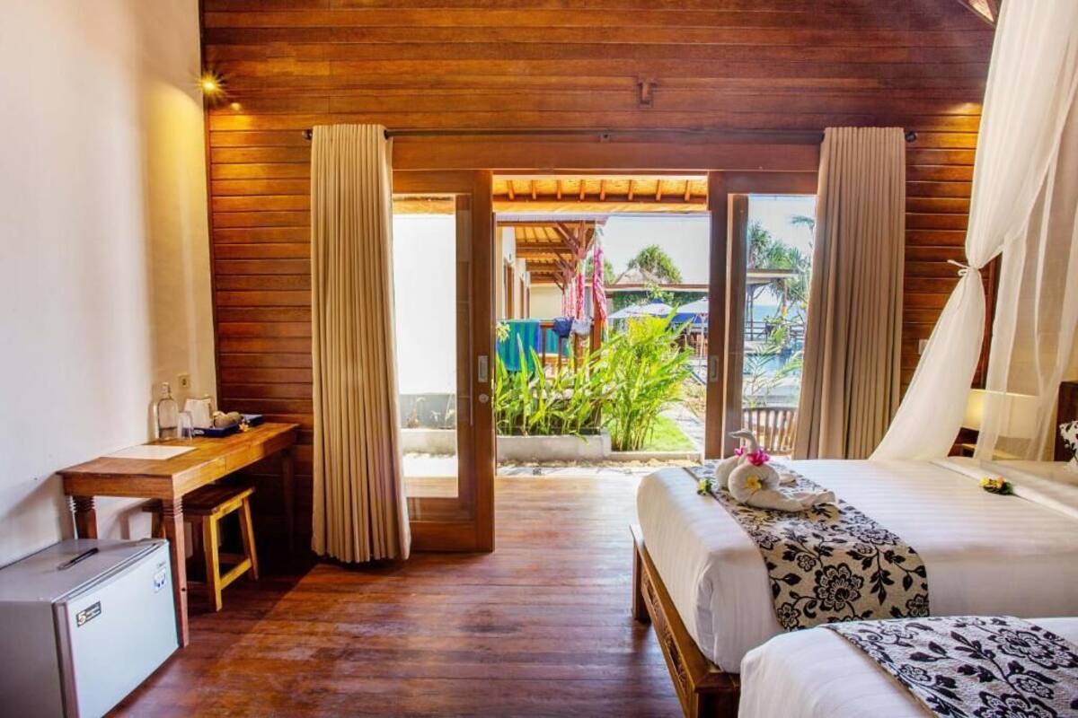 Quarto de hotel com teto de madeira, cama com colcha florida, escrivaninha com computador e vista para área externa.