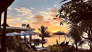 A poolside area with umbrellas, lounge chairs, and a view of the sunset over the water. - Nusa Veranda Sunset Villas & Restaurant (Ceningan Island)
