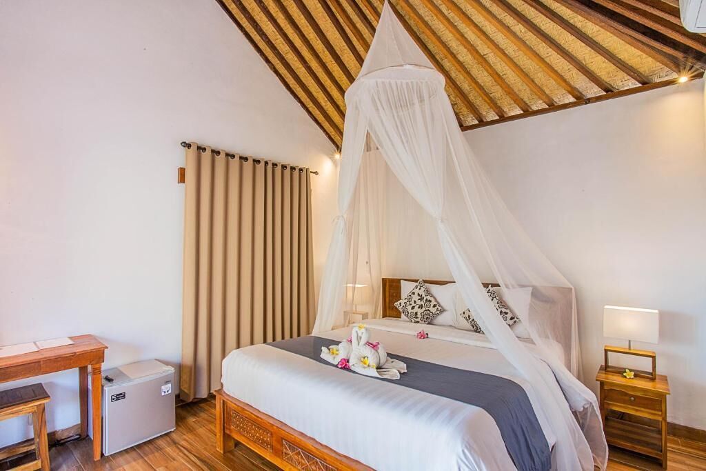 A bedroom with a canopy bed, a bedside table, a nightstand, a desk, and a small refrigerator.