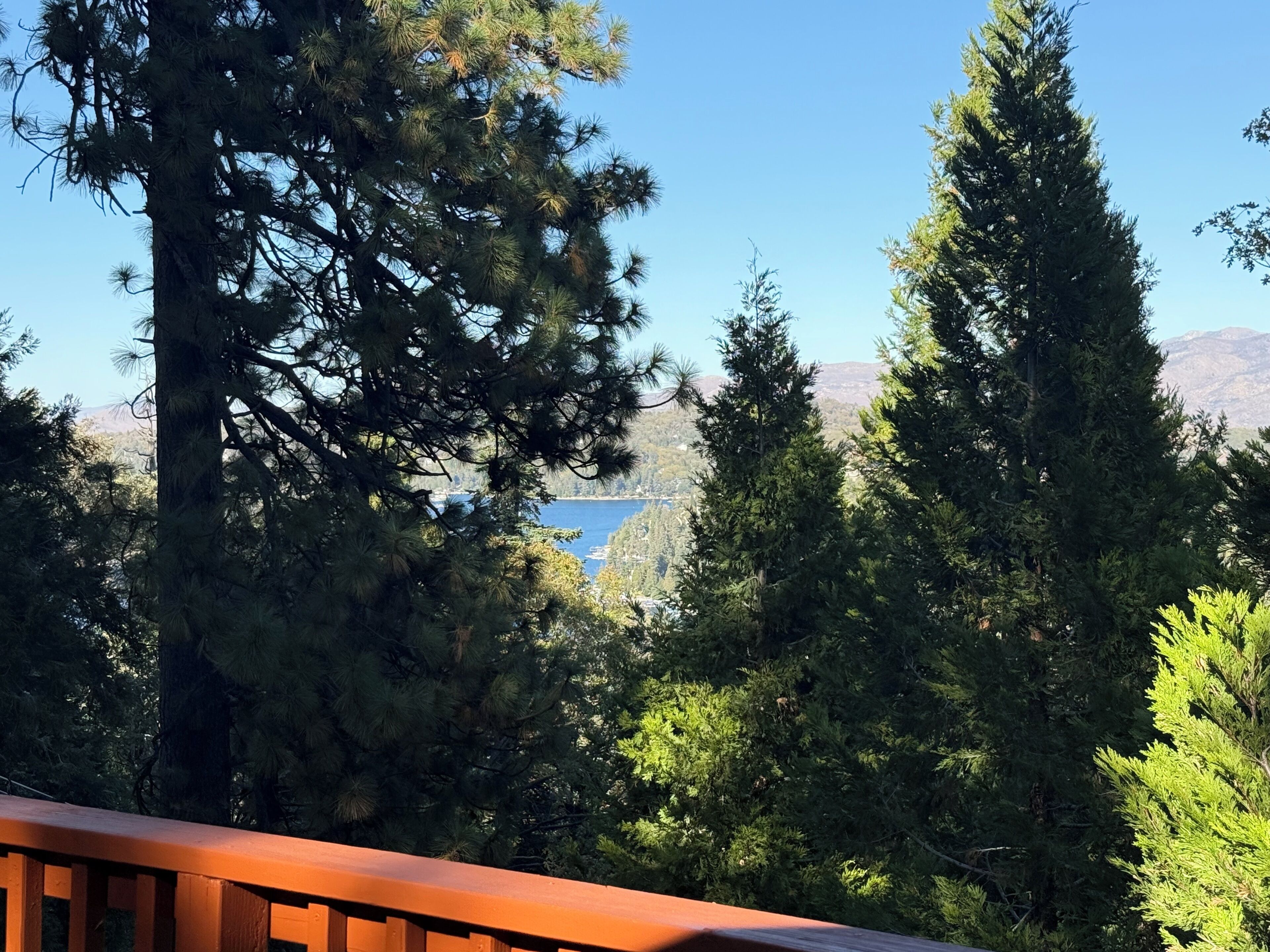 Blick von einem Balkon mit Holzwertung auf ein Gewässer und eine Berglandschaft.