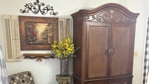 Un dormitori amb un llit, un armari de fusta, una cadira, una decoració mural i un ram de flors.