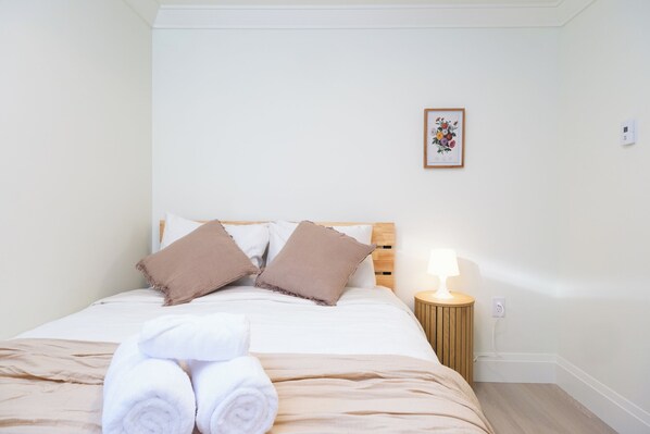 Un lit bien fait, avec des serviettes pliées, une lampe de chevet et un tableau encadré accroché au mur.