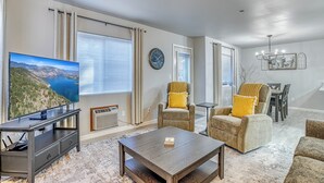 Een woonkamer met een flatscreen televisie, twee fauteuils, een salontafel en een eethoek met een kroonluchter.