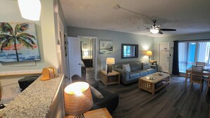 Un vaste salon comprenant un canapé, une table basse et un coin repas avec des chaises. On y trouve également un ventilateur de plafond, une lampe et des œuvres d’art accrochées aux murs.
