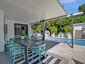 Un área de estar al aire libre, techada, con piscina, una mesa y sillas.