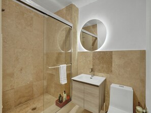 Un baño moderno con cabina de ducha de vidrio, un lavabo blanco y un mueble de tocador de madera.