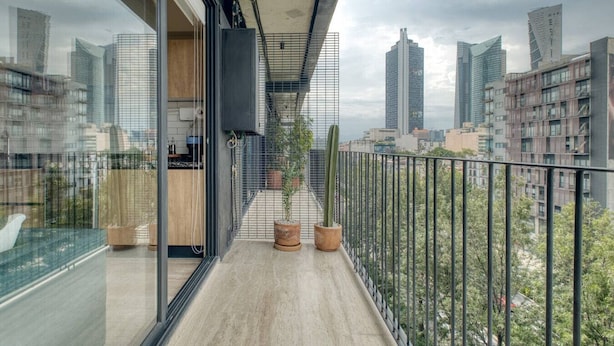 A modern balcony with a city view, a glass door, and potted plants. - MYLA - Loft - Chapultepec HighF (Mexico City)