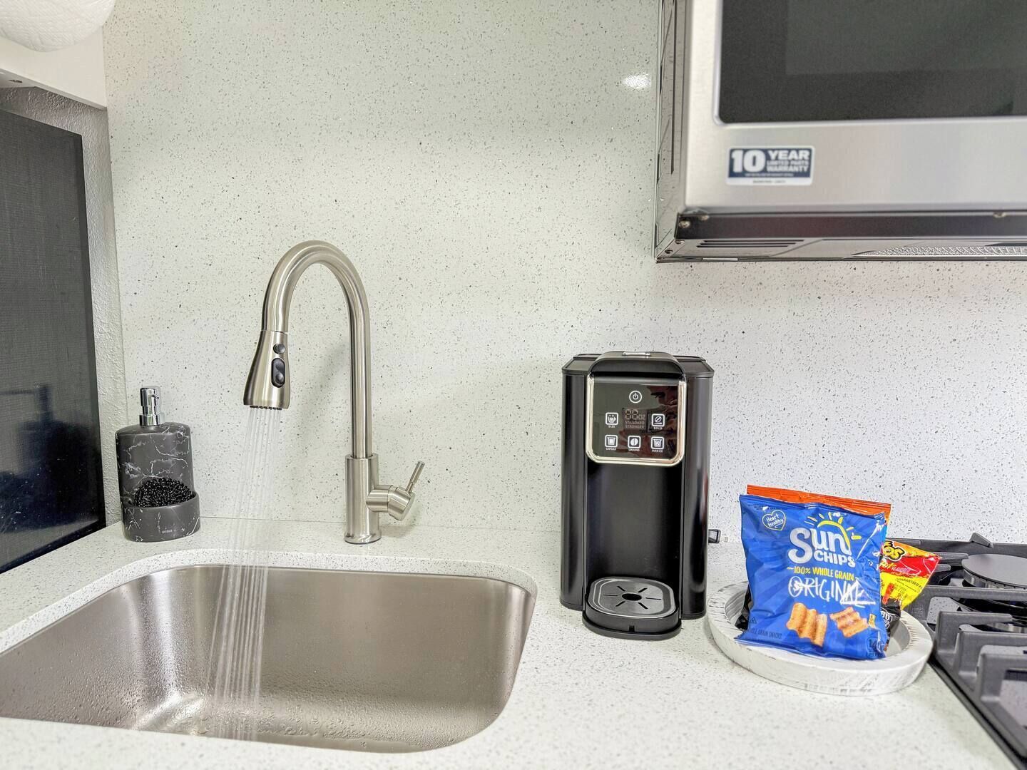 A kitchen with a stainless steel sink, a coffee maker, a bag of Sun Chips, and a microwave.
