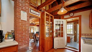 A kitchen with wooden cabinets, a brick wall, and a dining area visible through an open door. - Quiet Oceanfront Cottage with Dock (Boothbay Harbor)