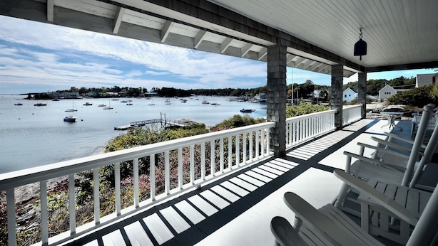 A covered porch with white railings overlooking a marina with boats. - Quiet Oceanfront Cottage with Dock (Boothbay Harbor)