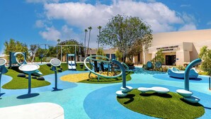 An outdoor play area with exercise equipment and a building labeled "Civic Center Library" in the background.