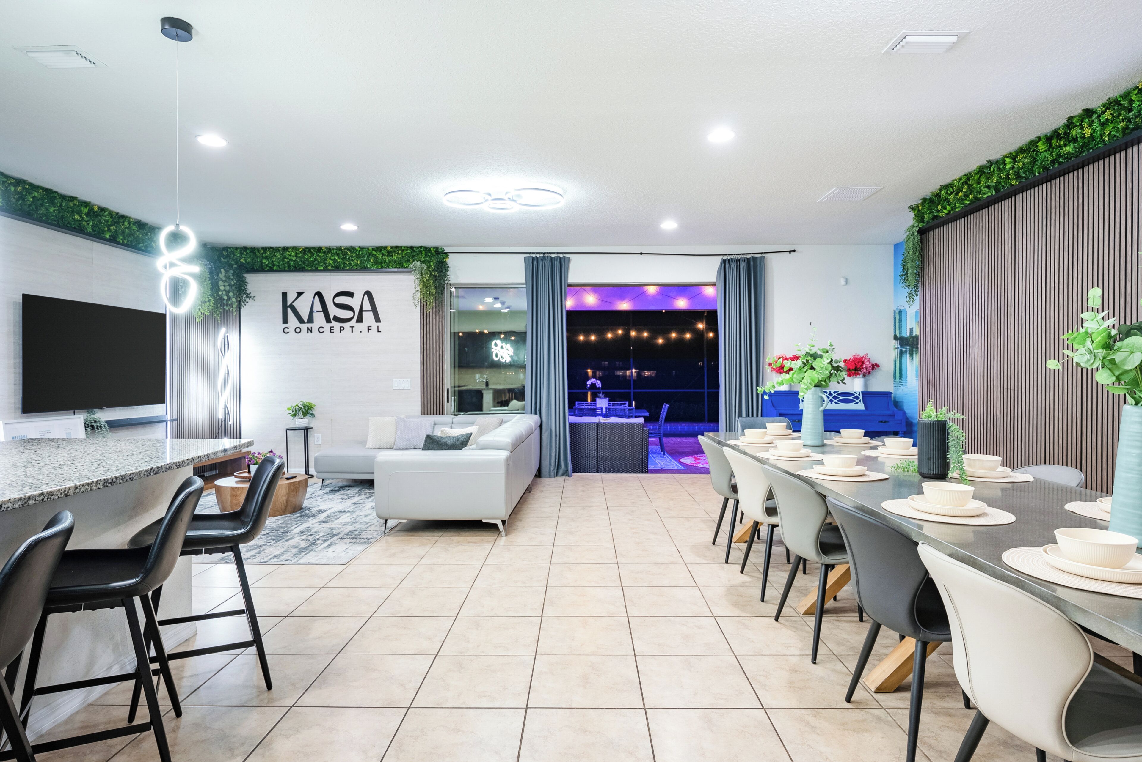 A modern kitchen with a bar area, a dining space with a long table, and a living area with a sofa.