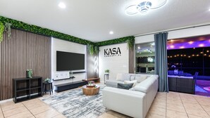 Ein modernes Wohnzimmer mit Flachbildfernseher, einer Couch, einem Couchtisch und einem großen Fenster mit Vorhängen.