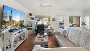A living room with a TV, a ceiling fan, a sofa, a coffee table, and a TV stand with plants. - Spacious and quiet 2-bedroom casita with view in Fountain Hills (Fountain Hills)