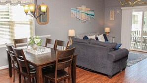 A dining area with a wooden table and chairs, a gray sofa, and a chandelier. - Heatherston 1063 Walk to Tee Time Daily overlooking the pool area! (Myrtle Beach)